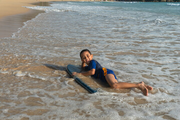 A boy lay down on body board while the wave move to the beach..Paradise beach blue sea, and clear sand landscape. .waves crashing on the beach background..smiling face of happy boy relax concept.