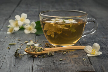 Jasmine flowers and flower tea in a glass bowl on a wooden table.A cup of flower tea and a wooden...