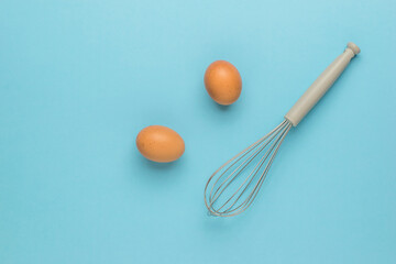 Two brown eggs and a whisk for whipping on a blue background.