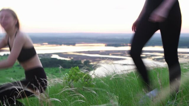 Two young women in sports clothes running around the field and sits down in the grass