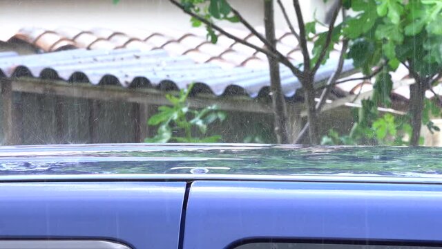 Soft focus of Heavy Rain Falling on the Roof of a Blue Ludospace Car