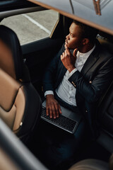 Pensive black employee working on laptop inside of car