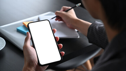 Businesswoman holding smart phone and making note on notebook.