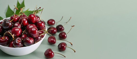 Fresh sour cherries in a bowl on green background.
