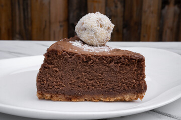 Sweet dessert. Closeup of a slice of chocolate cheesecake with a coconut truffle, in a white plate. 