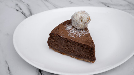 Delicious dessert. Top view of a chocolate cheesecake with a coconut truffle, on a white dish on the marble table. 