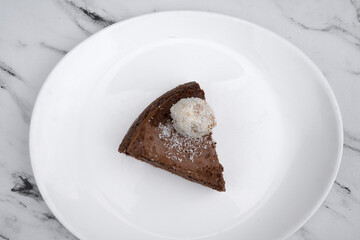 Delicious dessert. Top view of a chocolate cheesecake with a coconut truffle, in a white dish on the marble table.