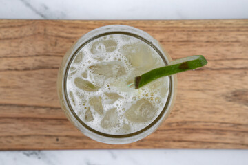 Tropical drinks. Top view of a Caipirinha cocktail with ice and lime on a wooden dish on a white marble table. 