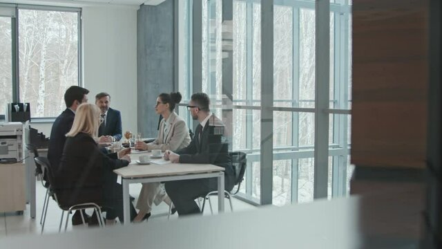 Panning wide shot with slowmo of team of professional lawyers and their chief sitting at negotiating table discussing legal matters