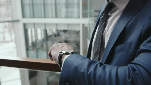 Midsection slowmo of unrecognizable business man or lawyer in suit and tie looking at expensive watch on his wrist standing indoors in modern office
