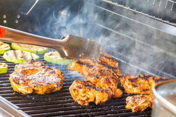 Turning juicy chicken steaks and grilled zucchini slices prepared on a modern garden grill