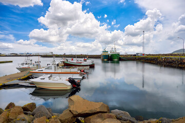 Port in a small village in the Icelandic countryside with several boats moored Blue sky and beautiful clouds reflected in the water. The scenery is bright and fresh and quiet.