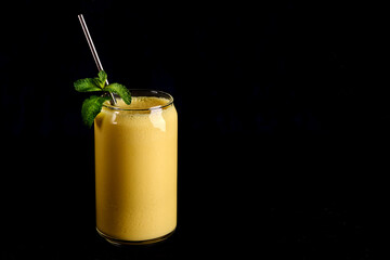 Mango lassi in glass with tube on black background. Traditional Indian and Pakistan drink with...