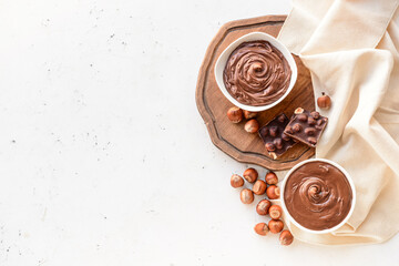 Bowls with tasty chocolate paste and hazelnuts on light background