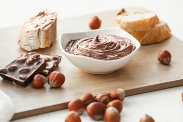 Bowl with tasty chocolate paste and hazelnuts on light background