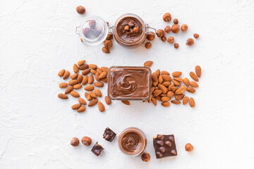 Bowl and jars with tasty chocolate paste and nuts on light background