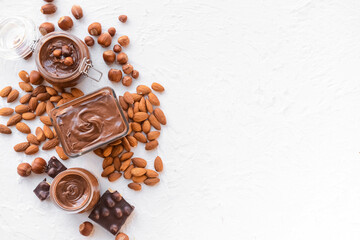 Bowl and jars with tasty chocolate paste and nuts on light background