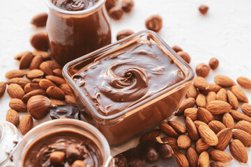 Bowl and jars with tasty chocolate paste and nuts on light background