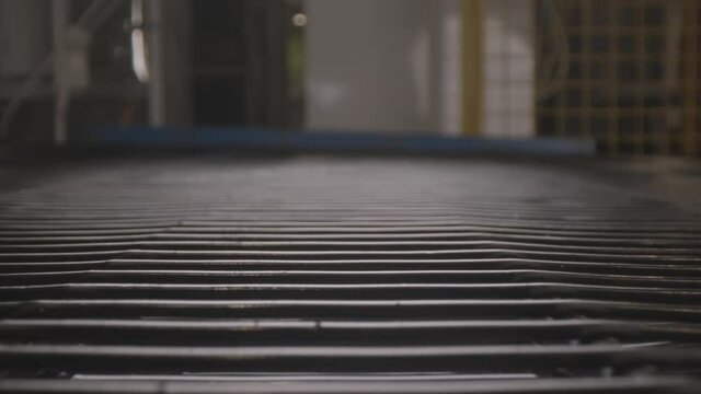 Empty conveyor belt made of thin metal tubes moves in semi-dark refrigerator production plant workshop extreme close view