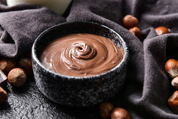 Bowl with tasty chocolate paste and hazelnuts on dark background