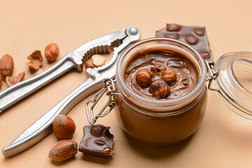 Jar with tasty chocolate paste and hazelnuts on color background