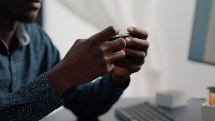 Close up of black man hands playing online internet mobile video games on his phone at home. Leisure entertainment time, gaming in free time on web services