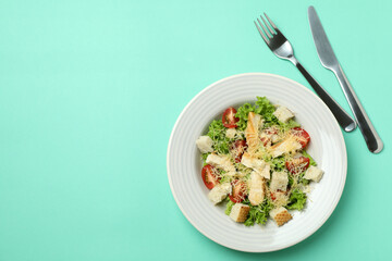 Plate with Caesar salad on mint background