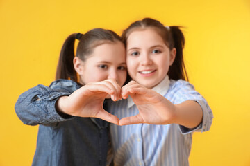 Cute twin girls making heart shape with their hands on color background