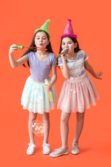Cute twin girls in party hats blowing soap bubbles on color background