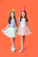 Cute twin girls in party hats on color background