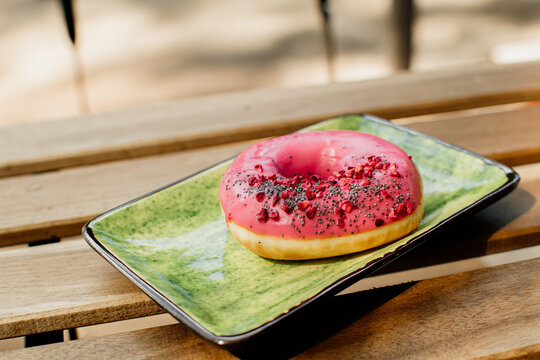 Sweet and colorful pink donut close-up on a green plate. Summer terrace in a cafe