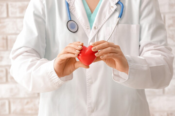 Female cardiologist with red heart near brick wall, closeup
