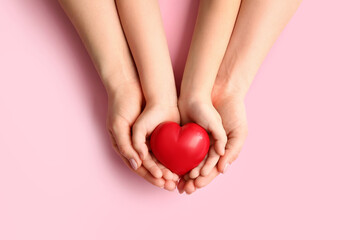 Hands of woman and child with red heart on color background