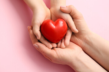 Hands of woman and child with red heart on color background, closeup