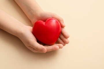 Child's hands with red heart on color background, closeup