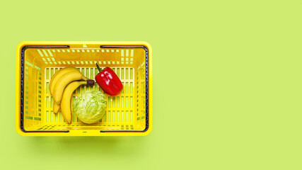 Shopping basket with cabbage, bananas and bell pepper on color background