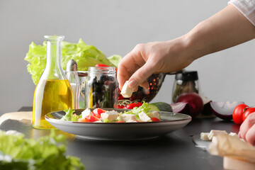 Woman preparing tasty Greek salad on table against grey background