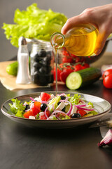 Woman pouring oil from bottle into plate with tasty Greek salad on table