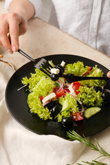 Woman eating tasty Greek salad at table, closeup