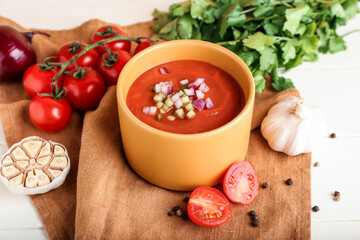 Bowl with tasty gazpacho and vegetables on light wooden background