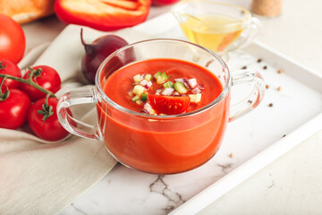 Glass pot with tasty gazpacho on light background