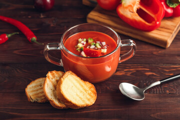 Glass pot with tasty gazpacho and bread slices on wooden background