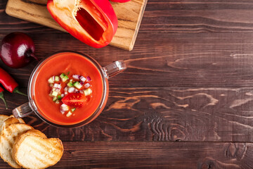 Glass pot with tasty gazpacho and bread slices on wooden background