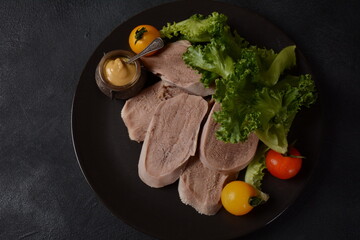 Sliced Beef Tongue Slices on a platter with lettuce leaves, cherry tomatoes and Dijon mustard on a...