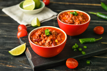 Bowls with delicious chili con carne on dark wooden background