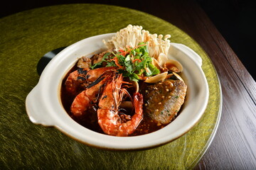 asian premium banquet menu braised seafood combo with big prawn , fish, shell and mushroom in hot clay pot on gold background dining table