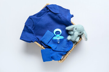 Basket with baby clothes, pacifier and toy on light background