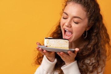 Young fit curly woman holding a piece of cake against yellow background