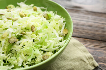 Bowl with tasty cabbage salad on wooden table, closeup