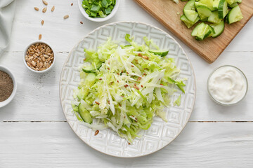 Plate with tasty cabbage salad and ingredients on light wooden table